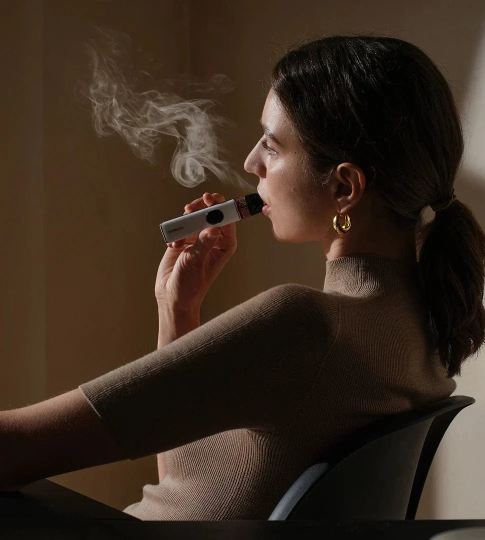 Woman using a vape pen with smoke visible, sitting against a neutral background Vaporesso XROS 5 30W Pod Kit